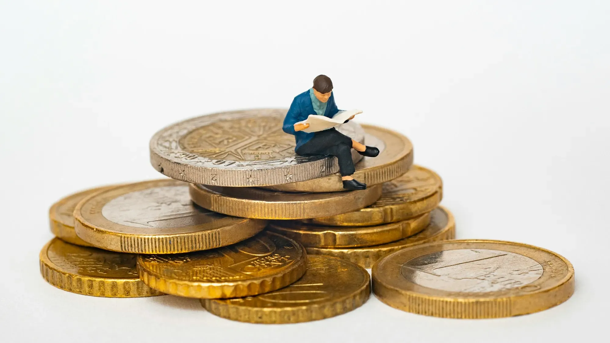 Persona en miniatura sentada sobre una pila de monedas leyendo el periódico