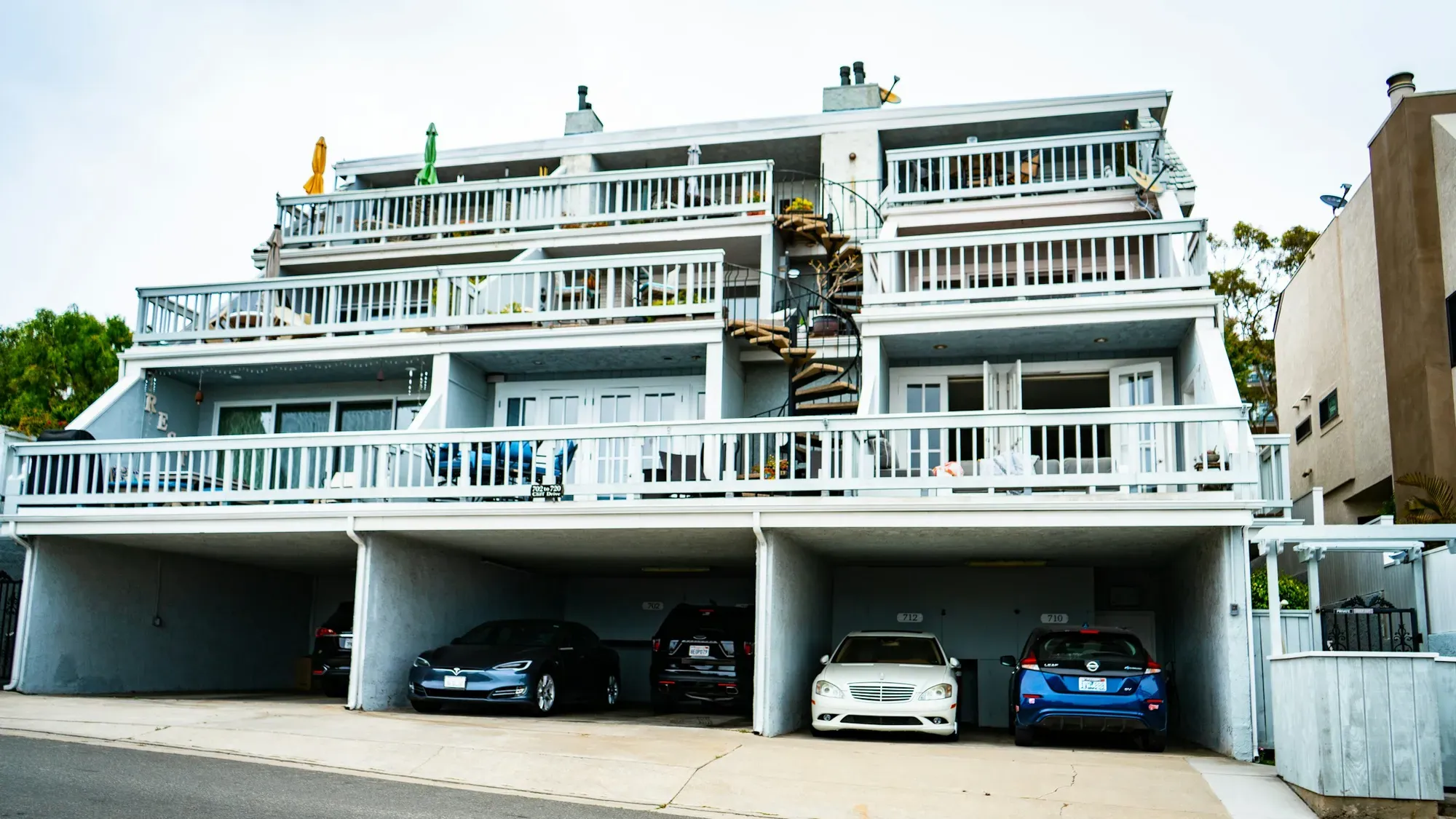 Edificio residencial blanco con parqueaderos cubiertos en el primer piso y varios carros estacionados